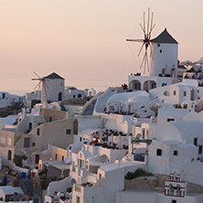 Sunset over white windmills in  town of Oia and panorama to Santorini island, Thira, Cyclades, Greece
