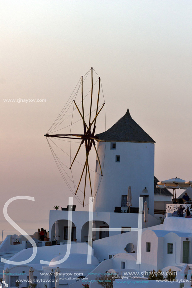 Sunset over white windmills in  town of Oia and panorama to Santorini island, Thira, Cyclades, Greece