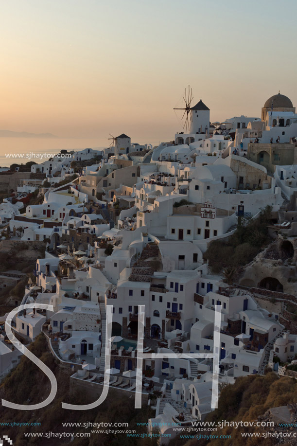 Sunset over white windmills in  town of Oia and panorama to Santorini island, Thira, Cyclades, Greece