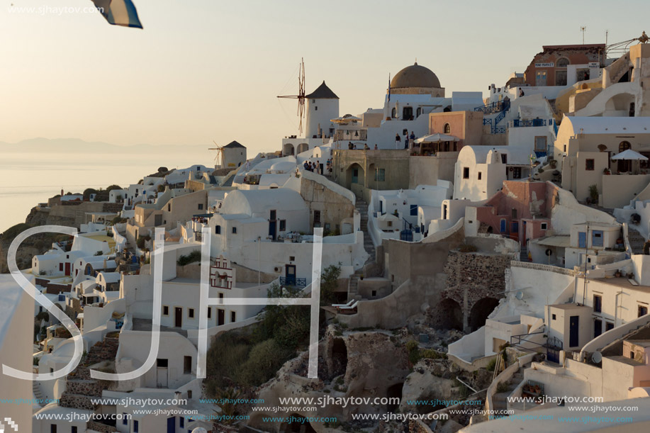 Sunset over white windmills in  town of Oia and panorama to Santorini island, Thira, Cyclades, Greece